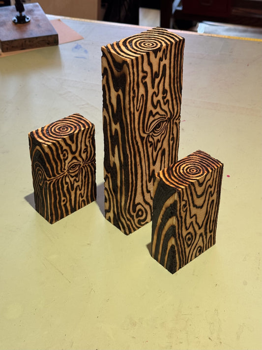 Three wood-burned blocks of different heights standing together on a workbench, burned grain lines wrapping every face